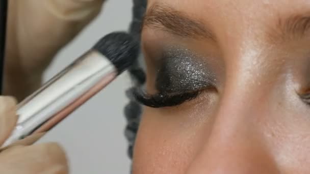 Макияж художник делает модели дымчатыми глазами с помощью специальной кисти серого тени для век, глаз и ресниц девушки вблизи зрения. Высокая мода . — стоковое видео