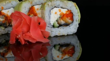Yeşil Ejderha suşi rulo ve pembe zencefil. Somon, sebze ve avokado closeup suşi roll. Japonya Restoran Menü siyah bir arka plan ayna yüzeyinde. Studio Japon mutfağı