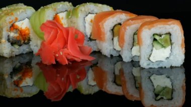 Ahşap bambu Çin yemek çubukları renkli suşi rulo koymak ve siyah bir arka plan ayna yüzeyinde zencefil. Studio Japon mutfağı