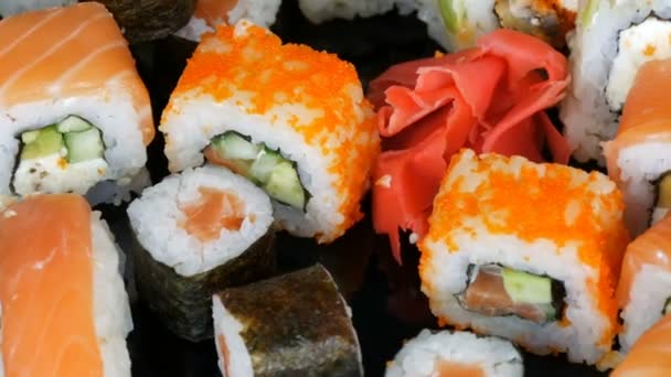 各种彩色寿司卷和生姜在镜面上的黑色背景旋转。一室公寓内的日本料理 — 图库视频影像