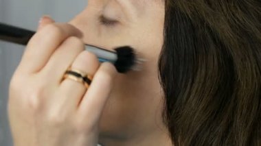 Sanatçı makyaj mavi gözlü orta yaşlı kadına vurgulayıcı kapatıcı ile makyaj yapmak. Yaş makyajı. Yakın çekim portre. Fırça ile tozu Uygula