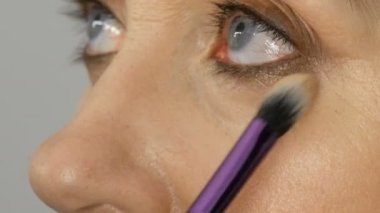 Sanatçı makyaj mavi gözlü orta yaşlı kadına vurgulayıcı kapatıcı ile makyaj yapmak. Yaş makyajı. Yakın çekim portre. Fırça ile tozu Uygula