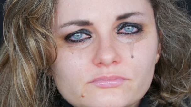 Beautiful young unhappy woman crying, washing off makeup. Real tears running down on girl face that screams of desperation in hysterics in a black jacket on a black background, face close up view — Stock Video