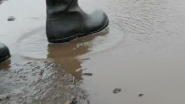 Bir adam kauçuk botlarda çamurlu su birikintisi boyunca yürür.