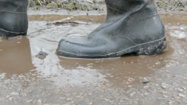 Мужчина проходит через грязную лужу в резиновых сапогах . — стоковое видео