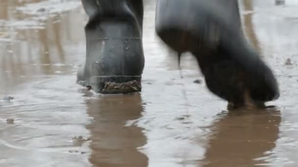 Um homem caminha pela poça enlameada com botas de borracha . — Vídeo de Stock