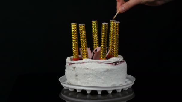 Las manos de las mujeres encienden velas en un hermoso pastel blanco dulce y elegante con mermelada de cereza decorada con crema y copos de coco en la parte superior. Tarta de cumpleaños sobre fondo negro . — Vídeo de stock