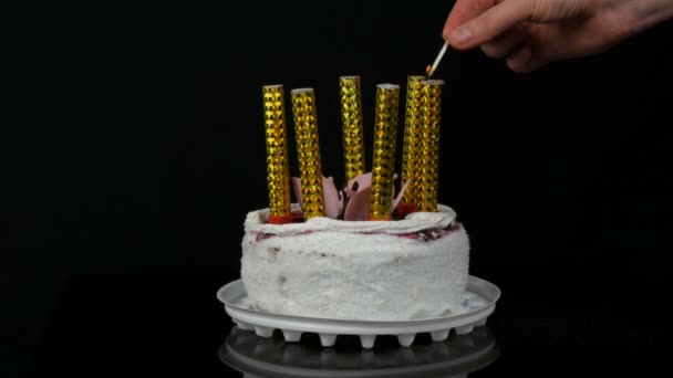 Las manos de las mujeres encienden velas en un hermoso pastel blanco dulce y elegante con mermelada de cereza decorada con crema y copos de coco en la parte superior. Tarta de cumpleaños sobre fondo negro . — Vídeos de Stock