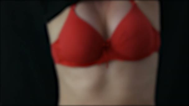Розмита сексуальна жінка знімає чорну футболку, під якою червоний бюстгальтер на чорному тлі — стокове відео