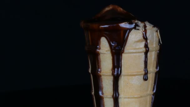 Melting ice cream on which pours chocolate syrup sauce on black background — Stock Video