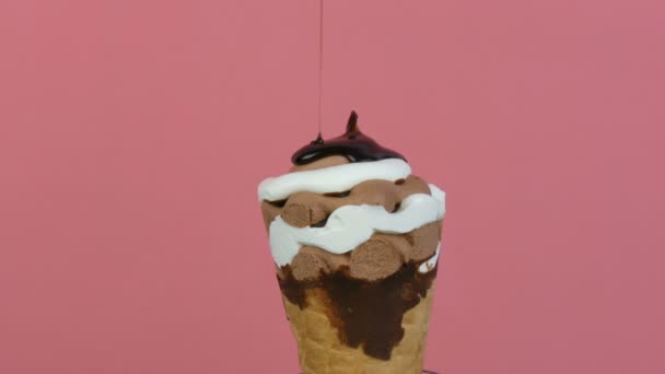 Chocolade saus glazuur stroomt over ijs in een wafel kopje op roze achtergrond — Stockvideo