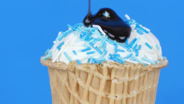 Chocolate sauce icing flows over ice cream in a waffle cup on blue background — Stock Video
