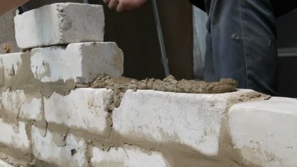 Constructor masculino colocando ladrillo blanco sobre cemento y pared de pie. Manos del hombre colocando ladrillos de construcción vista de cerca — Vídeo de stock