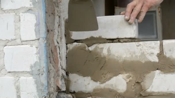 Αρσενικό οικοδόμος για το λευκό τούβλο στο τσιμέντο και στέκεται τοίχο. Τα χέρια του ανθρώπου που χτίζει τούβλα κοντά στη θέα — Αρχείο Βίντεο