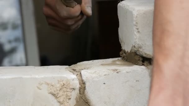 Constructor masculino colocando ladrillo blanco sobre cemento y pared de pie. Manos del hombre colocando ladrillos de construcción vista de cerca — Vídeo de stock