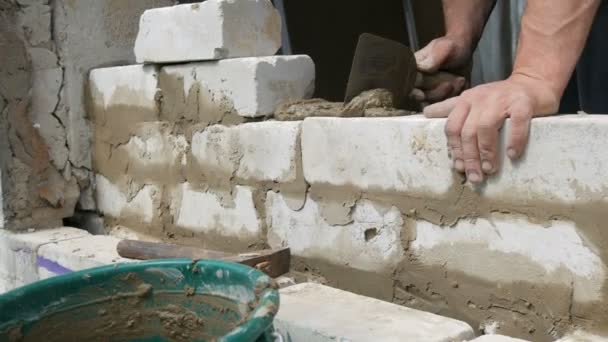 Mannelijke bouwer het leggen van witte baksteen op cement en staande muur. Handen van de mens leggen gebouw bakstenen close-up uitzicht — Stockvideo