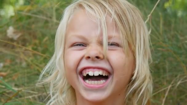 Portrait d'une jolie blonde aux yeux bleus et souriante de sept ans avec un enfant au visage sale dans une rue à l'extérieur de la ville un jour d'été — Video