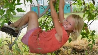 Yedi yıllık komik kirli çocuk kız sarışın yaz günü şehir dışında bir ağaç dalı üzerinde asılı