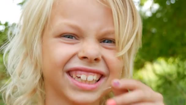 Portrait d'une jolie blonde aux yeux bleus et souriante de sept ans avec un enfant au visage sale dans une rue à l'extérieur de la ville un jour d'été — Video