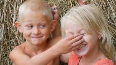 Komik kirli yüzleri sarışın erkek ve kız kardeşi çocuklar ile mutlu etrafında aptal, bir yaz günü dışında köyde samanlıkların arka planda birbirlerine yüzler ve boynuzları yapmak