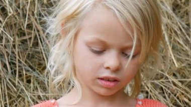 Samanlıkların arka planında saman larla oynayan kız. Sevimli bir gülümseme portresi ve bir yaz günü şehir dışında bir sokakta kirli bir yüz çocuk ile mavi gözlü sarışın yedi yaşındaki kız gülmek