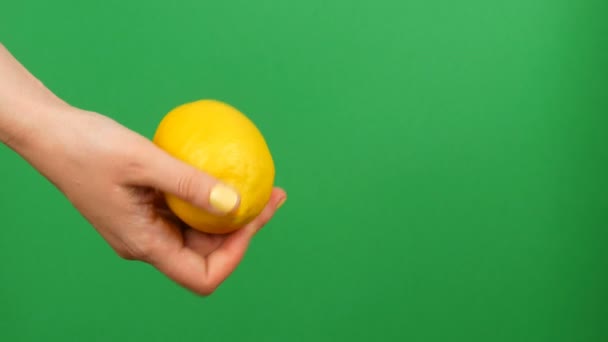 Vrouwelijke hand met gele manicure houdt een citroen op groene Chroma Key achtergrond — Stockvideo