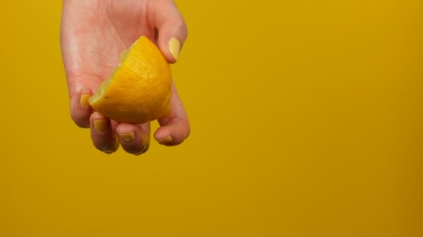 La mano femenina con la manicura amarilla exprime medio limón sobre el fondo amarillo — Vídeos de Stock