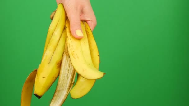 Mano femenina con manicura amarilla sostiene la cáscara de plátano sobre un fondo verde clave de cromo — Vídeos de Stock