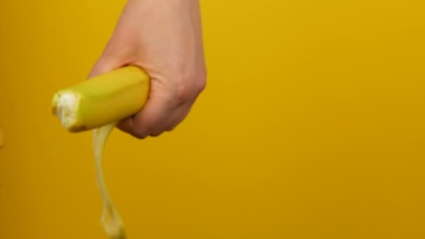 weibliche Hand mit gelber Maniküre schält die Schale einer reifen Bananenfrucht auf gelbem Hintergrund