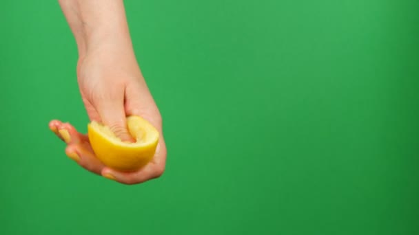 Mano femenina con manicura amarilla exprime medio limón sobre fondo de croma verde — Vídeo de stock