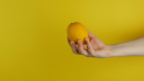 Vrouwelijke hand met gele manicure houdt een citroen op gele achtergrond — Stockvideo