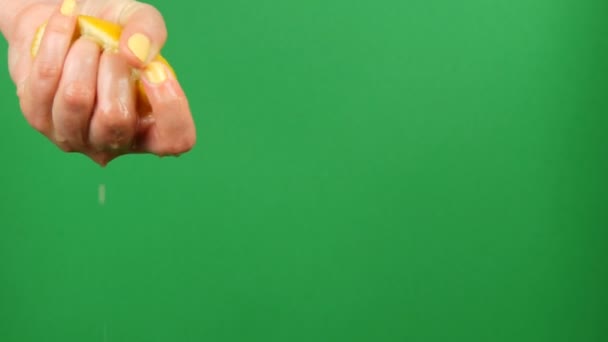 Weibliche Hand mit gelber Maniküre presst eine halbe Zitrone auf grünem Chroma-Schlüsselhintergrund aus — Stockvideo