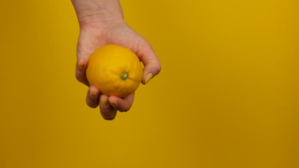 Mão feminina com manicure amarelo mantém um limão no fundo amarelo — Vídeo de Stock