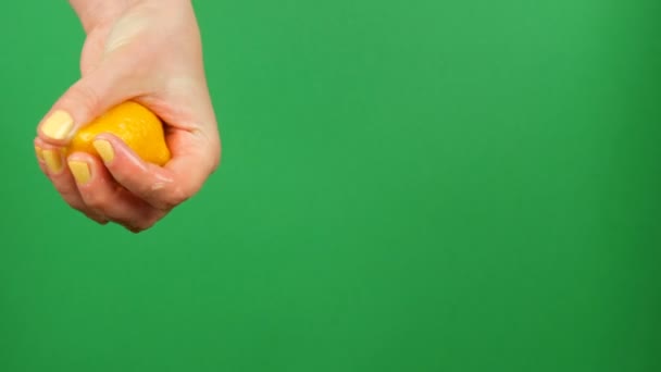 Θηλυκό χέρι με κίτρινο μανικιούρ συμπιέζει μισό λεμόνι στο φόντο πράσινη αποχρώσεων — Αρχείο Βίντεο