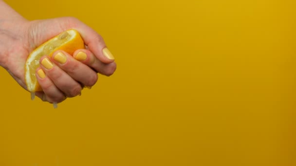 Vrouwelijke hand met gele manicure knijpt uit een halve citroen op gele achtergrond — Stockvideo