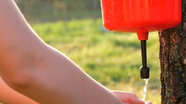 Nastolatek myje ręce pod plastikową umywalkę lub dozownik wody, a strumienie wody spływające ręce na tle zielonej trawy w ogrodzie letnim na zewnątrz. Dziecko zdrowe — Wideo stockowe