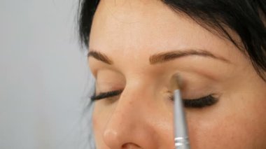 Özel fırça ile akşam kahverengi göz makyajı ve kaş yapıyor uzun siyah saçlı güzel bir mavi gözlü kadın modeli portresi