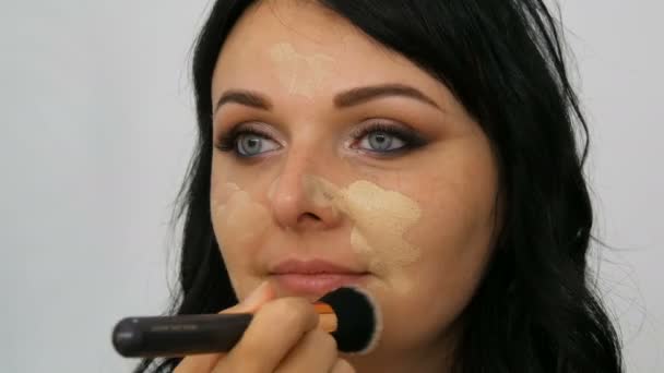 Styliste applique fond de teint sur le visage de la femme modèle dans un salon de beauté, maquillage du soir — Video