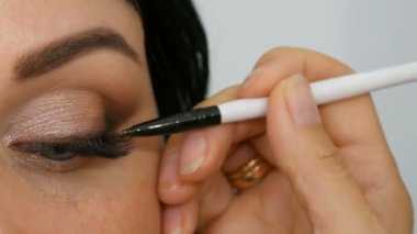 Özel fırça ile akşam kahverengi göz makyajı ve kaş yapıyor uzun siyah saçlı güzel bir mavi gözlü kadın modeli portresi