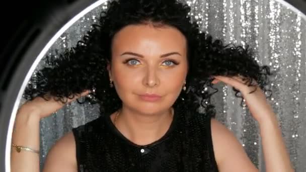 Belle jeune femme caucasienne brune aux cheveux noirs bouclés posant et souriant devant la caméra en studio — Video