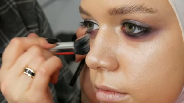 Ένας επαγγελματίας μακιγιέζ εφαρμόζει ένα κονσίλερ στο μοντέλο της κοπέλας με ειδική βούρτσα. Υψηλή μόδα, γυρίσματα βίντεο στο στούντιο — Αρχείο Βίντεο