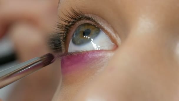 Alta costura. Maquillaje artista haciendo profesional maquillaje ojos ahumados de color rosa y negro para modelo de niña para disparar en el estudio. Vista de cerca del modelo de ojo verde — Vídeos de Stock