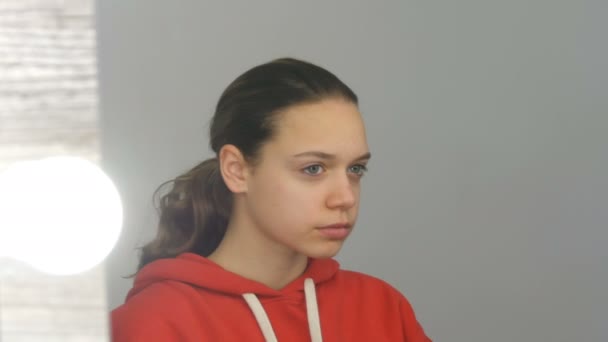 Teen flicka i röd tröja tittar in i kameran i studion — Stockvideo