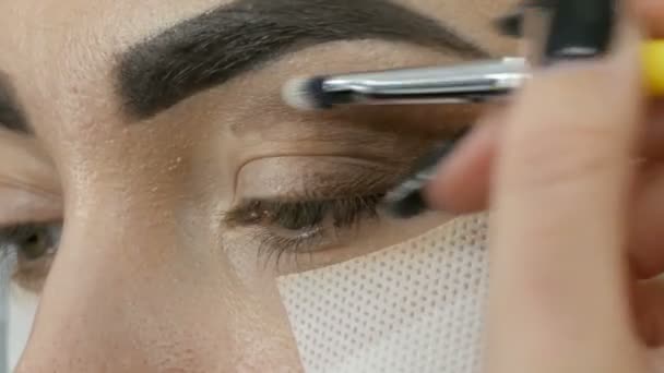 专业化妆师使一个美丽的模型的棕色阴影的化妆烟熏眼睛与绿色的眼睛关闭 — 图库视频影像
