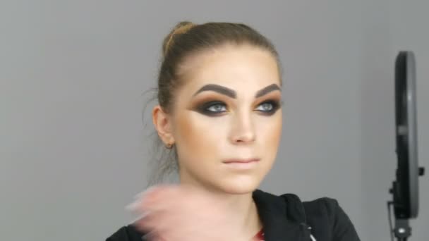 Krásná mladá dívka model s módní make-up nazývá kouřové oči je stojící před zrcadlem a dělá sama účes narovnat vlasy. — Stock video