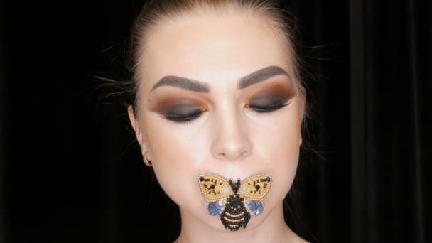 Retrato de una hermosa joven modelo con los ojos ahumados de moda maquillaje y una mariposa en sus labios posando delante de la cámara en el estudio. Alta costura — Vídeos de Stock