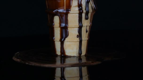 Melting ice cream on which pours chocolate syrup sauce on black background — Stock Video