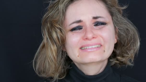 Beautiful young tearful unhappy woman crying washing off makeup. Real tears running down on face that screams of desperation in hysterics in black jacket on a black background, face close up view — Stock Video