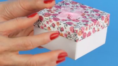 Bir çiçek baskı ve tırnakmavi bir arka plan üzerinde kırmızı oje ile boyanmış kadın elleri tarafından düzenlenen pembe bir yay ile küçük bir hediye kutusu
