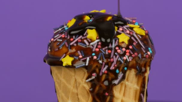 Chocolade saus glazuur stroomt over ijs in een wafel kopje op roze achtergrond — Stockvideo